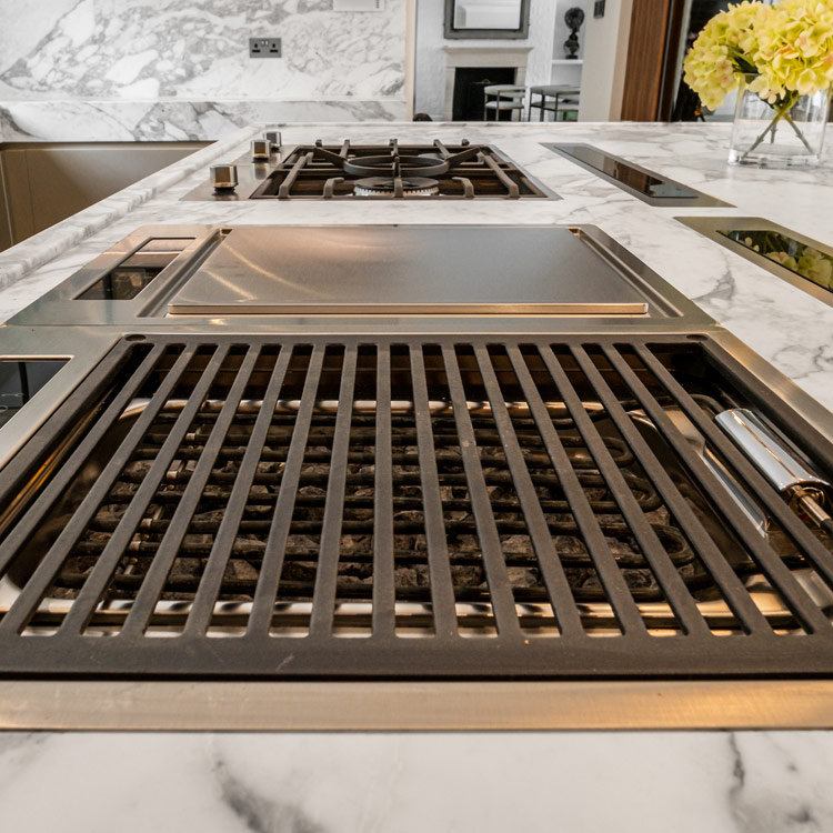 A BBQ grill and Teppanyaki grill sit alongside two gas burners on a generous kitchen island finished in Carrara marble. Italian luxury kitchen by Fontana London | Design as Art